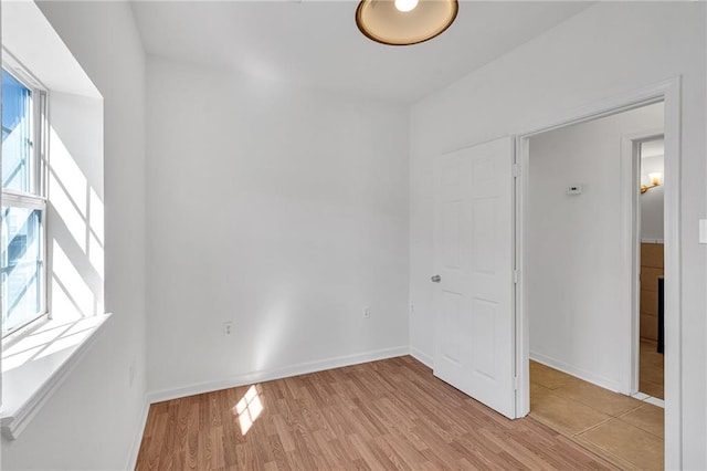 empty room featuring light wood-type flooring, plenty of natural light, and baseboards