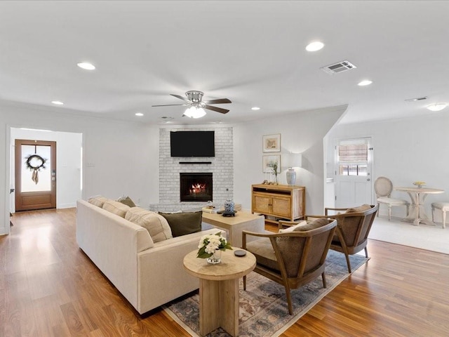 living room with light wood-style floors, a brick fireplace, visible vents, and recessed lighting