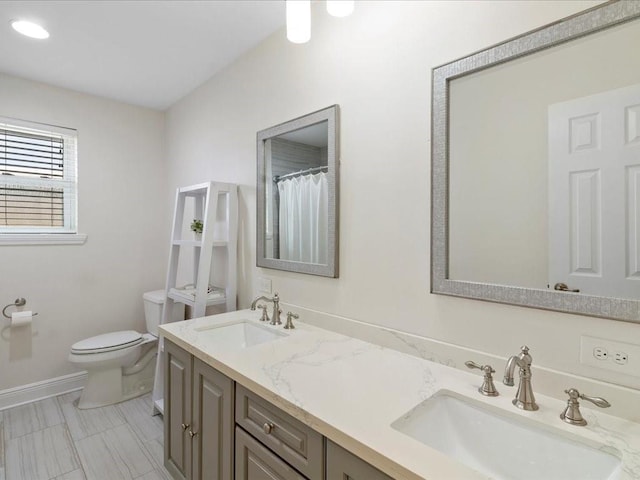 full bathroom featuring toilet, double vanity, baseboards, and a sink