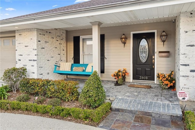 doorway to property featuring covered porch, brick siding, roof with shingles, and an attached garage