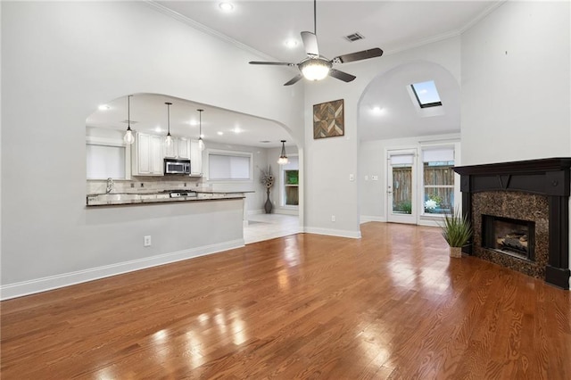 unfurnished living room featuring visible vents, a premium fireplace, ornamental molding, wood finished floors, and baseboards