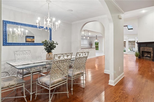 dining room with arched walkways, a fireplace, wood finished floors, baseboards, and crown molding