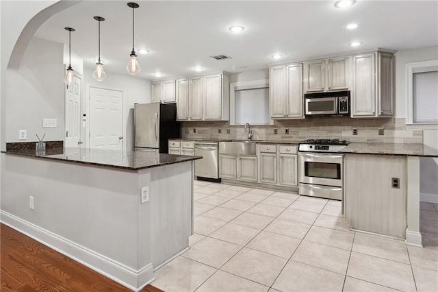 kitchen with stainless steel appliances, a peninsula, visible vents, dark stone counters, and tasteful backsplash