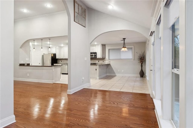 unfurnished living room with arched walkways, high vaulted ceiling, light wood-type flooring, and baseboards