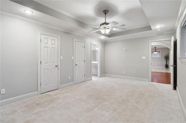 unfurnished bedroom featuring a raised ceiling, light colored carpet, ornamental molding, connected bathroom, and baseboards