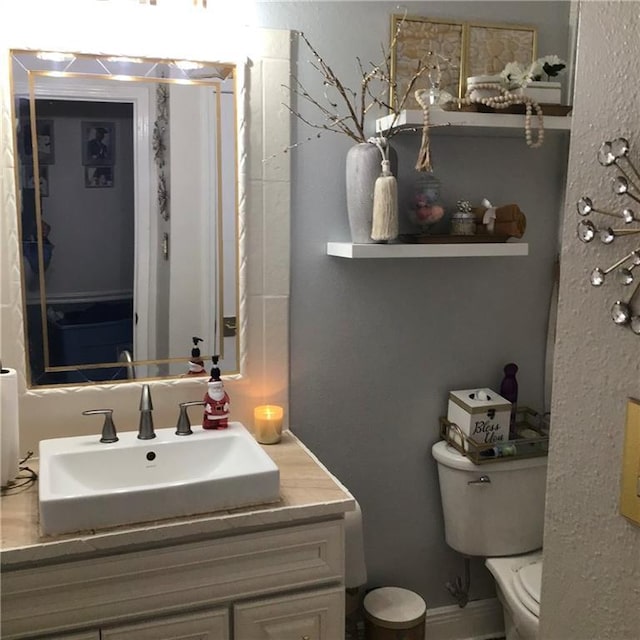 half bathroom featuring vanity, toilet, and baseboards