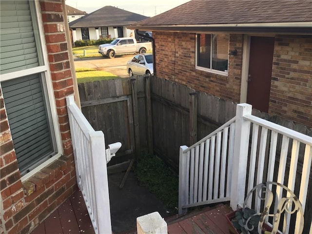 view of property exterior featuring roof with shingles, fence, and brick siding