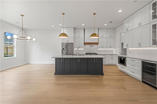 kitchen with wine cooler, a sink, white cabinetry, light countertops, and appliances with stainless steel finishes