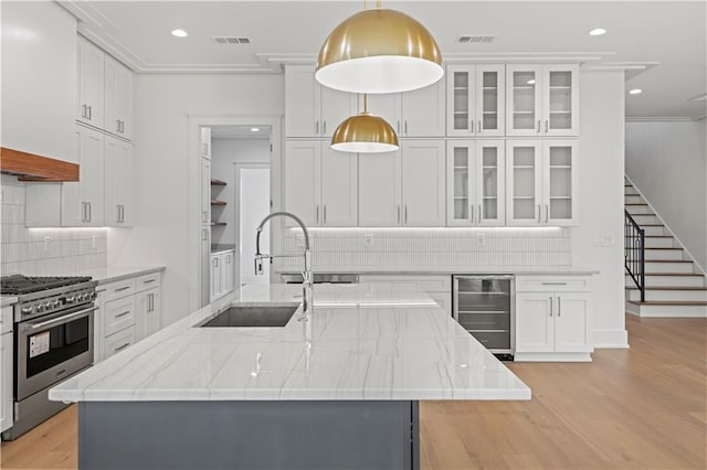 kitchen with beverage cooler, visible vents, high end stainless steel range oven, a kitchen island with sink, and light wood-style floors