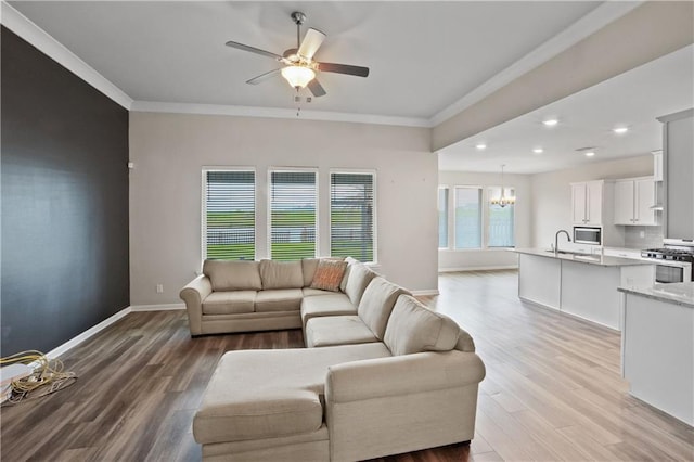 living room featuring crown molding, baseboards, wood finished floors, and ceiling fan with notable chandelier