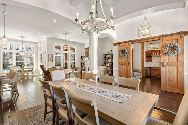 dining area featuring a barn door, dark wood-style flooring, decorative columns, and crown molding