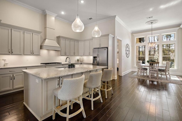 kitchen with visible vents, dark wood-type flooring, a sink, an island with sink, and stainless steel fridge