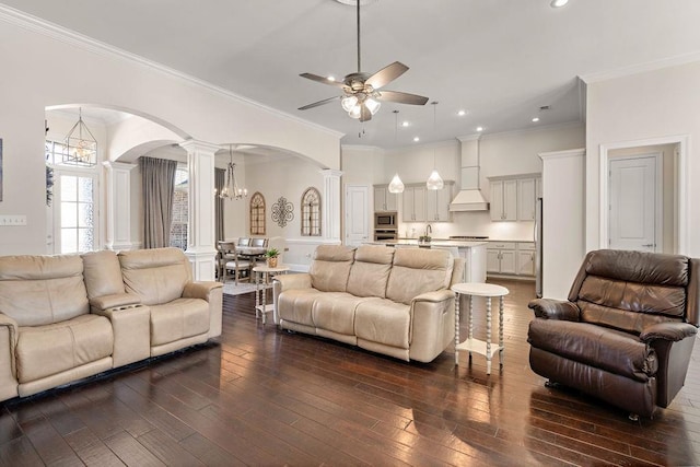 living area with arched walkways, recessed lighting, ceiling fan with notable chandelier, dark wood finished floors, and ornate columns