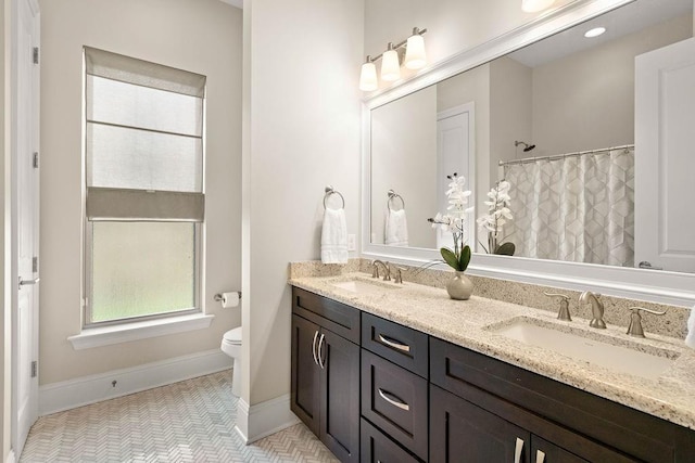 bathroom featuring toilet, double vanity, baseboards, and a sink