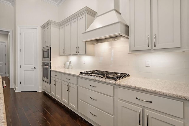 kitchen featuring premium range hood, dark wood-type flooring, ornamental molding, appliances with stainless steel finishes, and decorative backsplash