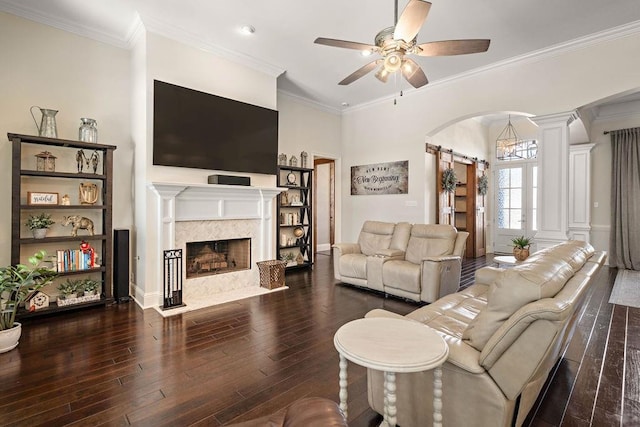 living area with arched walkways, a barn door, ornamental molding, ceiling fan, and wood finished floors