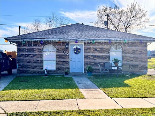 view of front of property featuring a front yard, roof with shingles, and brick siding