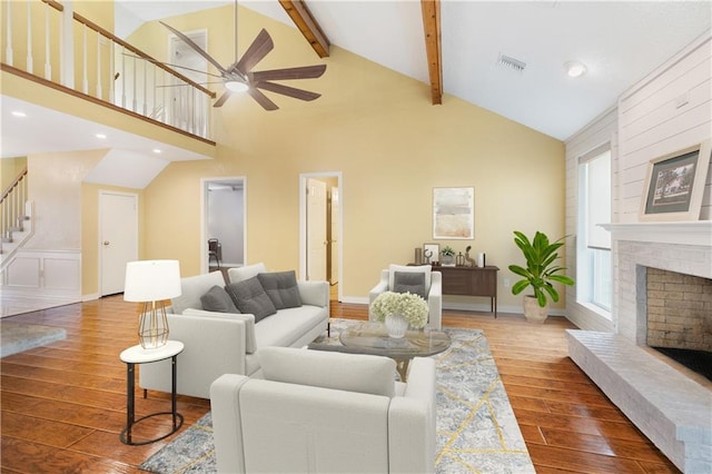 living room featuring visible vents, a fireplace with raised hearth, stairway, wood finished floors, and beamed ceiling