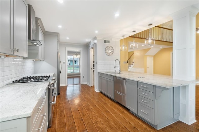 kitchen featuring gray cabinetry, a sink, appliances with stainless steel finishes, dark wood-style floors, and wall chimney exhaust hood