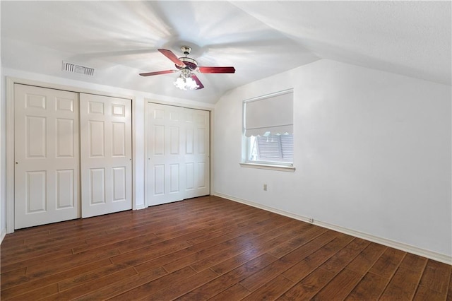 unfurnished bedroom with visible vents, dark wood finished floors, a ceiling fan, vaulted ceiling, and two closets