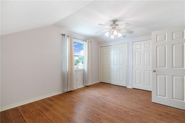 unfurnished bedroom with lofted ceiling, wood finished floors, visible vents, baseboards, and multiple closets