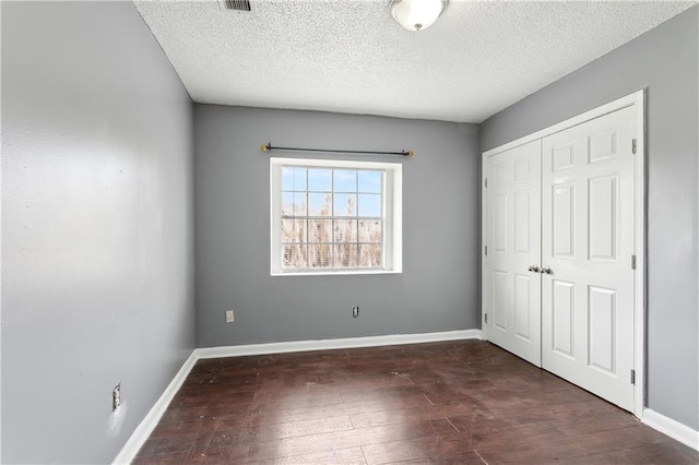 unfurnished bedroom featuring a textured ceiling, a closet, dark wood finished floors, and baseboards