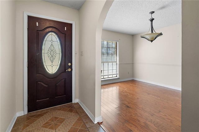 entryway featuring arched walkways, a textured ceiling, dark wood-style floors, and baseboards