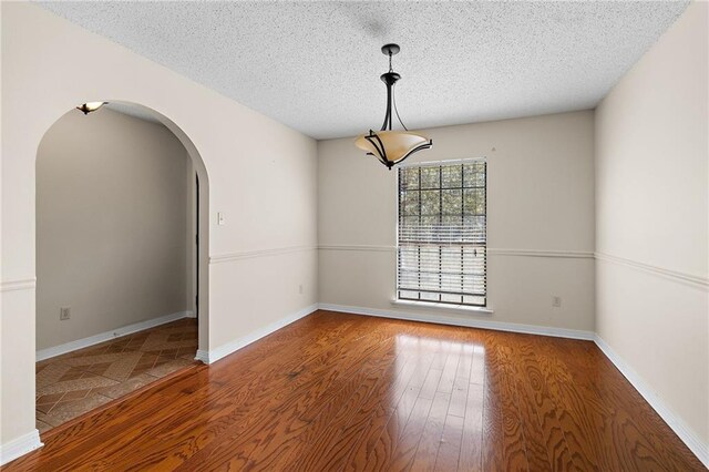 unfurnished room with baseboards, a textured ceiling, arched walkways, and wood finished floors