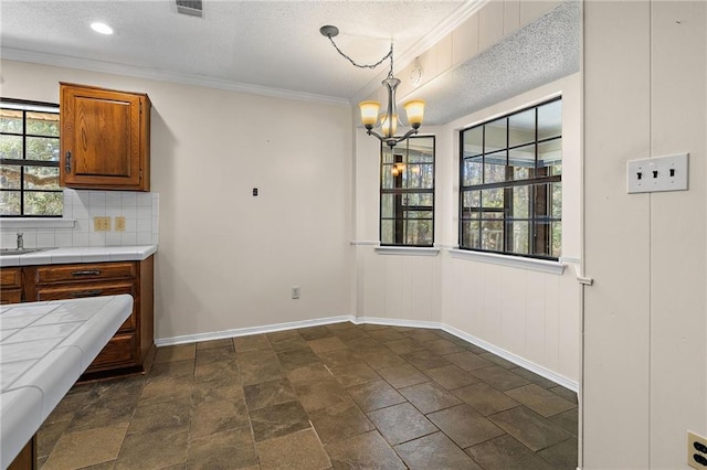 unfurnished dining area featuring crown molding, visible vents, a textured ceiling, a chandelier, and baseboards