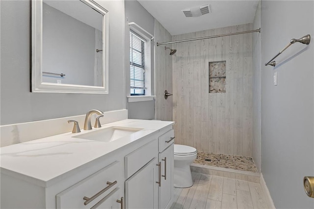 bathroom featuring visible vents, toilet, wood finished floors, a tile shower, and vanity