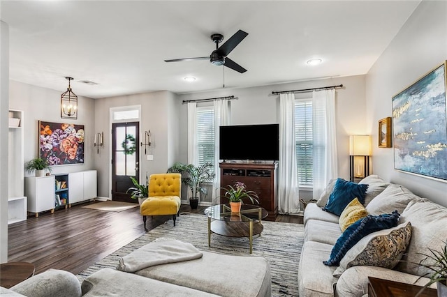 living area with ceiling fan with notable chandelier, wood finished floors, visible vents, and baseboards