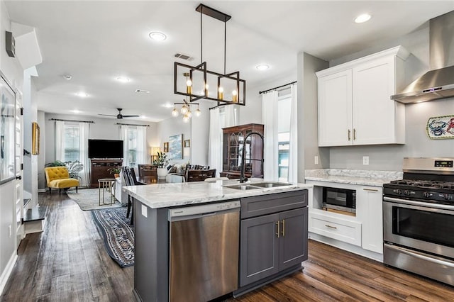 kitchen featuring a sink, white cabinets, open floor plan, appliances with stainless steel finishes, and wall chimney range hood