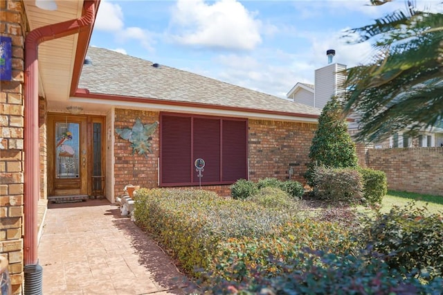 view of exterior entry featuring roof with shingles and brick siding