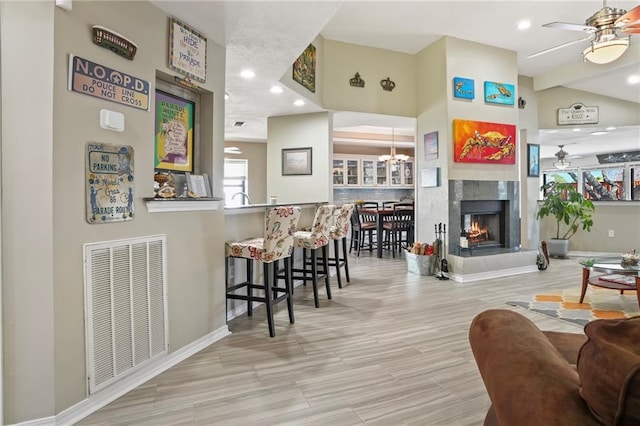 living room featuring a premium fireplace, visible vents, wood finished floors, and ceiling fan with notable chandelier