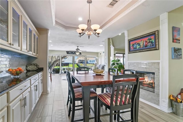 dining area with visible vents, a tile fireplace, ceiling fan with notable chandelier, a tray ceiling, and recessed lighting