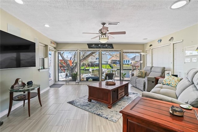 living area featuring a ceiling fan, visible vents, a textured ceiling, and baseboards