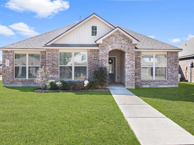 view of front of house featuring roof with shingles, a front lawn, and brick siding