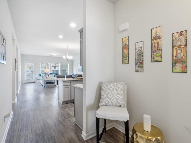 corridor featuring baseboards, dark wood-style flooring, a sink, and an inviting chandelier