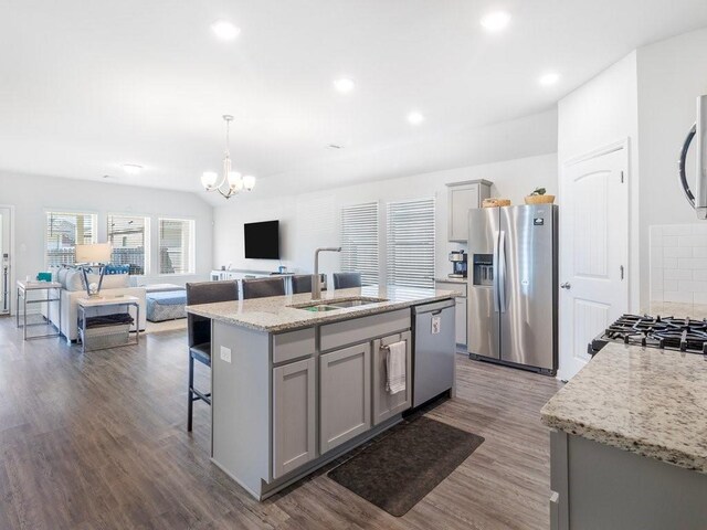 kitchen featuring gray cabinetry, stainless steel appliances, a sink, open floor plan, and dark wood finished floors