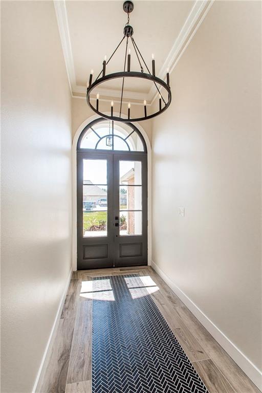 entryway featuring light wood finished floors, baseboards, crown molding, french doors, and a chandelier