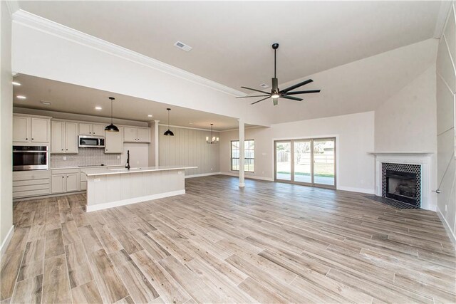 unfurnished living room featuring light wood finished floors, visible vents, a tiled fireplace, ornamental molding, and ceiling fan with notable chandelier