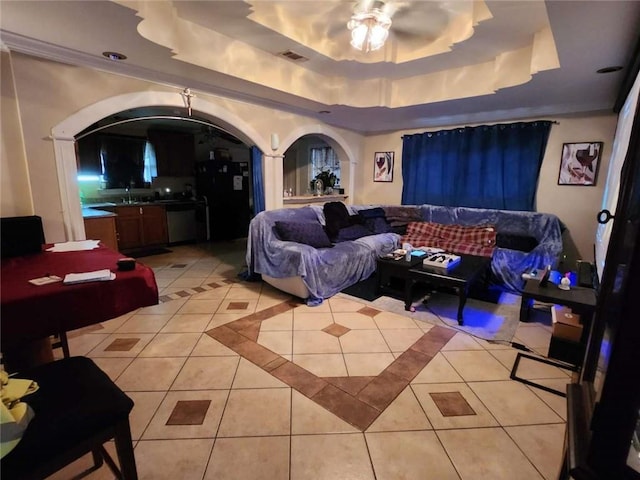 home theater room with arched walkways, light tile patterned floors, a raised ceiling, visible vents, and a ceiling fan