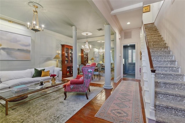 interior space featuring decorative columns, wood finished floors, an inviting chandelier, stairs, and a decorative wall