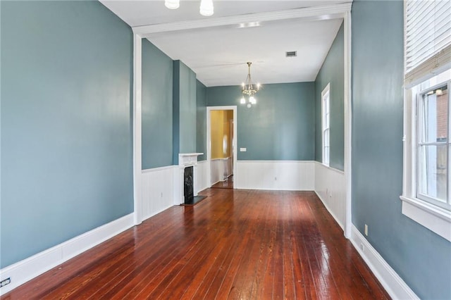 unfurnished room featuring hardwood / wood-style flooring, a wainscoted wall, a fireplace, visible vents, and an inviting chandelier