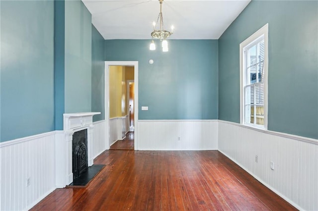 spare room featuring a chandelier, wainscoting, wood-type flooring, and a fireplace