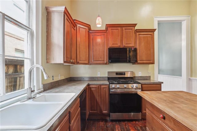 kitchen with brown cabinetry, wainscoting, black appliances, pendant lighting, and a sink