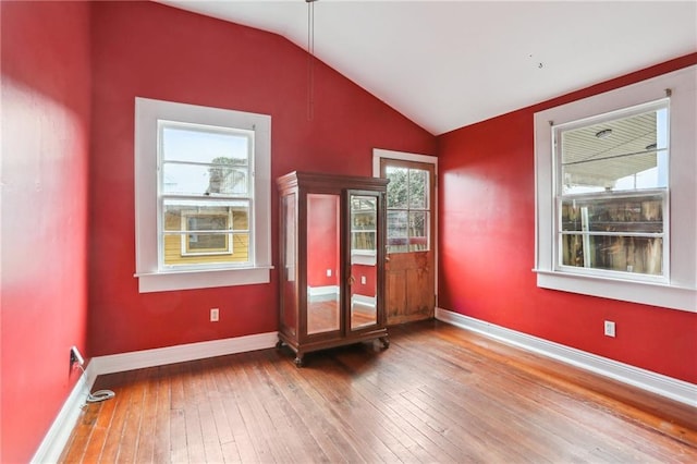 spare room with lofted ceiling, wood-type flooring, and baseboards