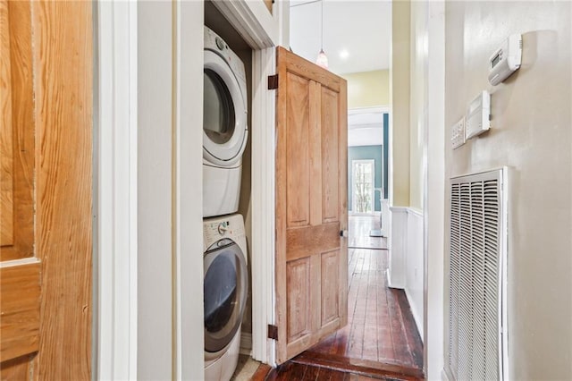 clothes washing area featuring laundry area, a heating unit, visible vents, hardwood / wood-style floors, and stacked washer / drying machine