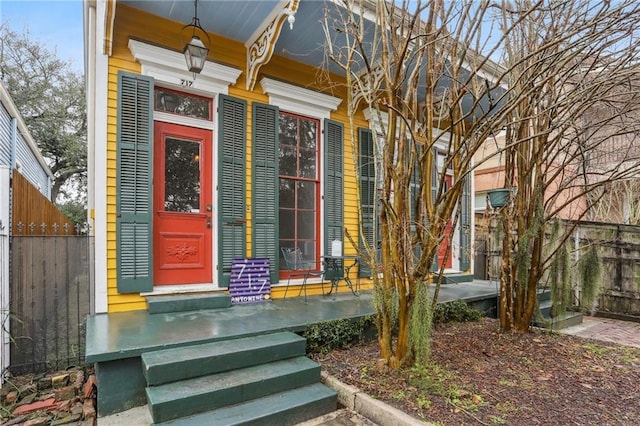 view of exterior entry featuring covered porch and fence