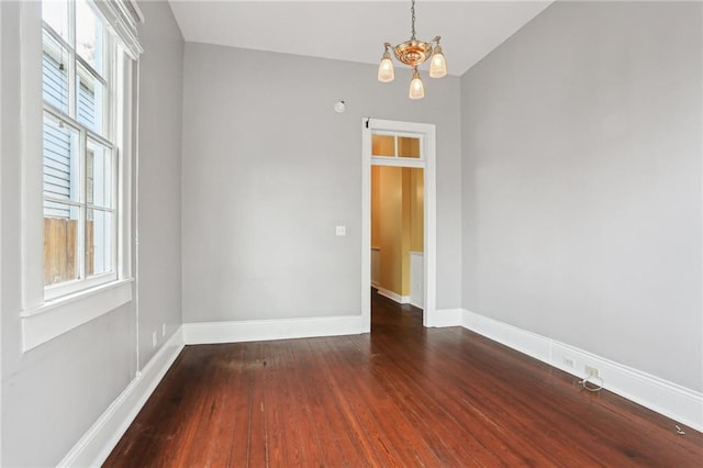 spare room with an inviting chandelier, baseboards, and wood finished floors